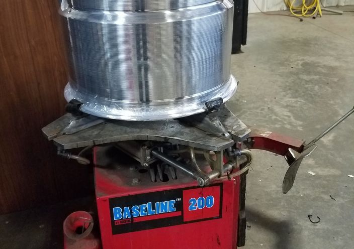 A metal vehicle wheel rim secured on a red Baseline 200 tire changing machine in a workshop. | Integrated Automotive