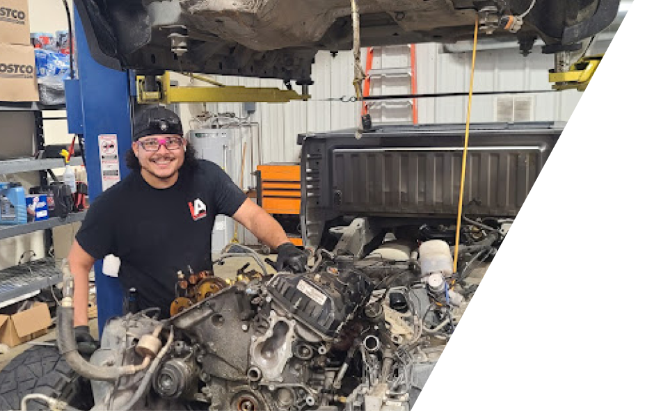 A smiling mechanic in a black shirt working on a truck engine in a repair shop. | Integrated Automotive