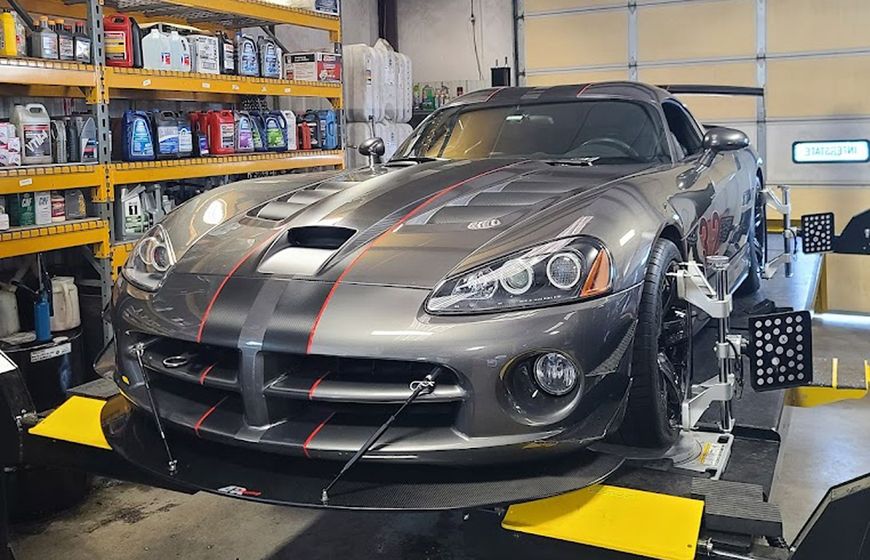 A gray Dodge Viper sports car with red racing stripes undergoing a wheel alignment in a brightly lit automotive garage. | Integrated Automotive