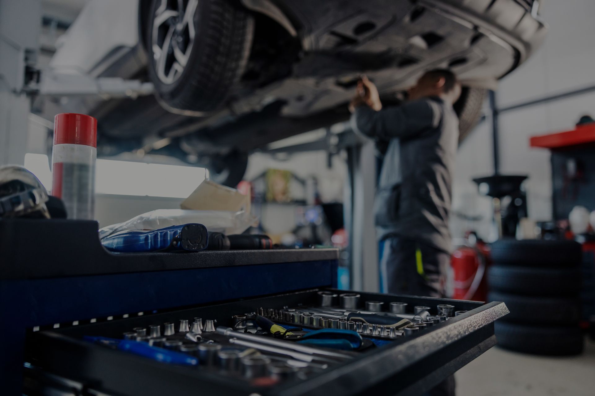 Mechanic working under a car in a repair shop, tools visible in foreground. | Integrated Automotive