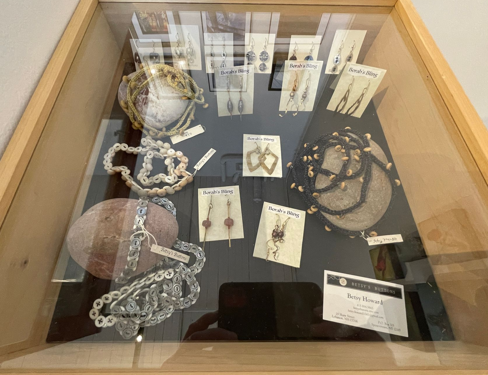 A display case featuring various pieces of handcrafted jewelry, including necklaces and earrings, set on a dark surface.