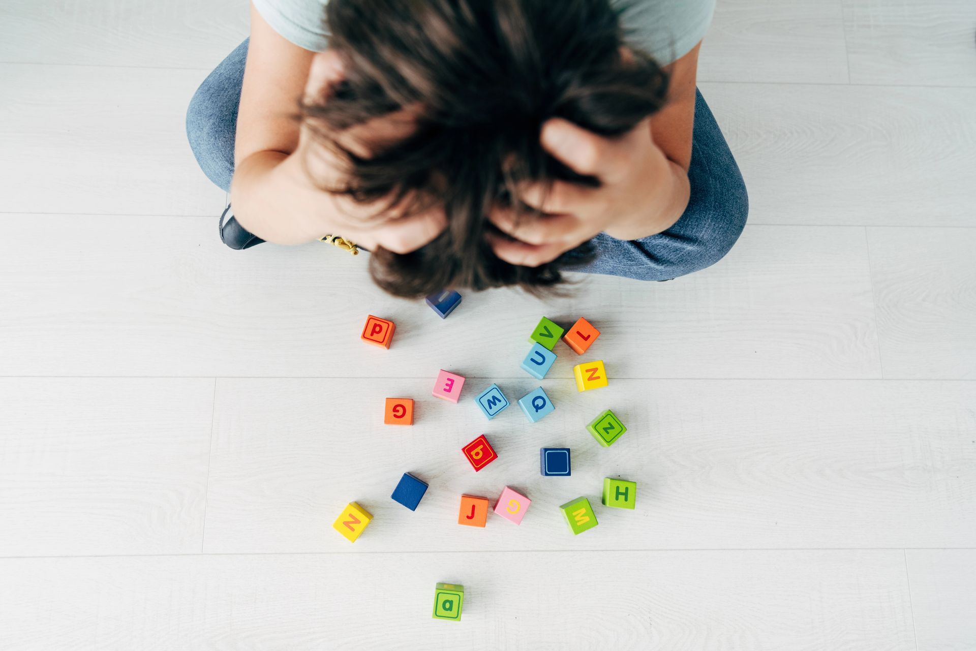 A child is sitting on the floor with his head in his hands surrounded by colorful letter blocks.