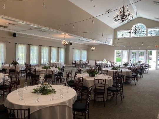 A large room with tables and chairs set up for a wedding reception. v