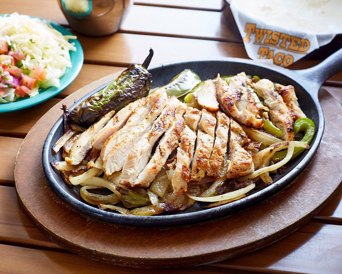 A skillet filled with twisted taco chicken fajitas , onions and peppers on a wooden table.