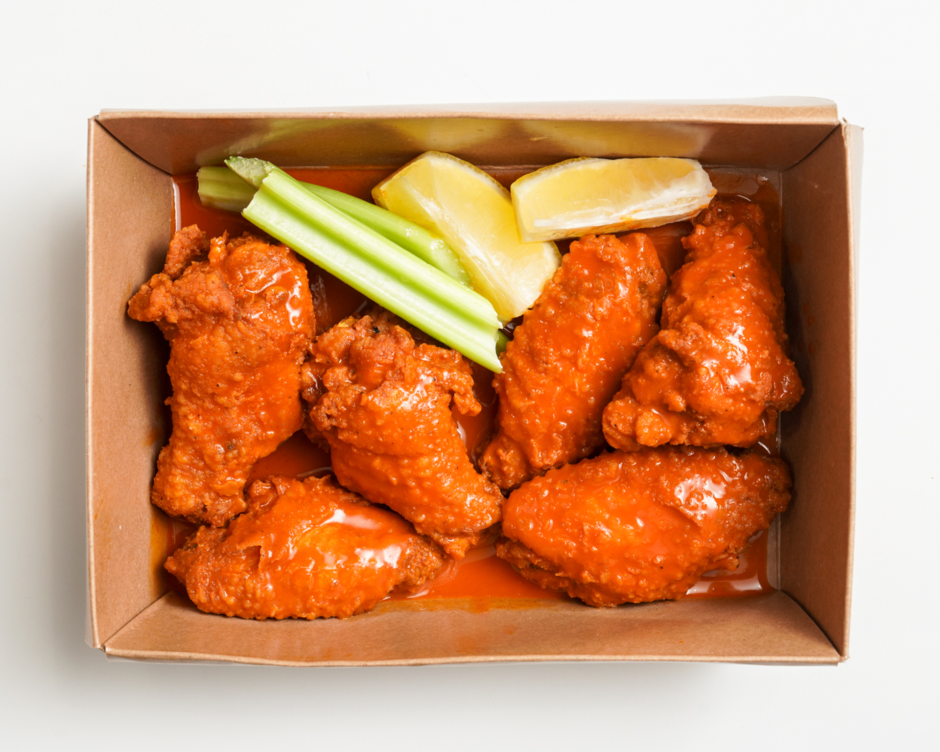 Buffalo chicken wings in a cardboard box, with celery and lemon wedges.