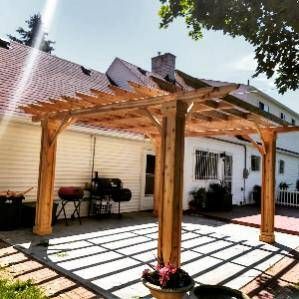 A wooden pergola is sitting on top of a patio in front of a house.