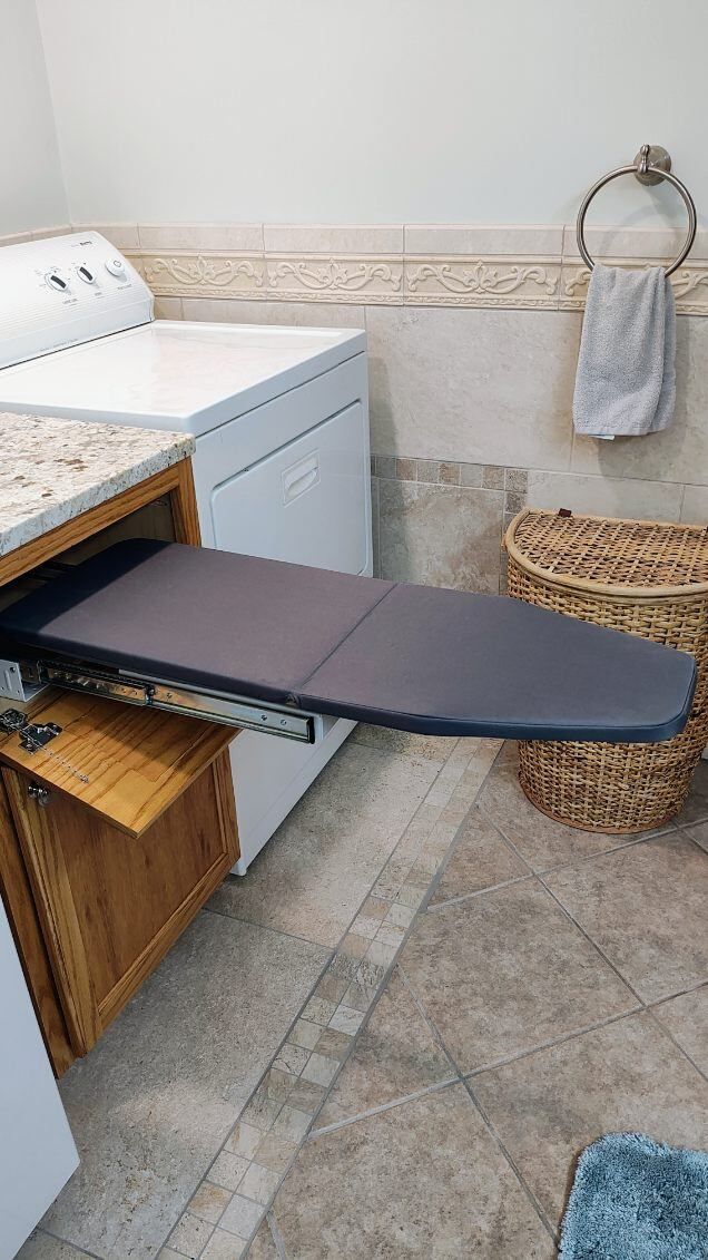 An ironing board is pulled out of a cabinet in a laundry room.