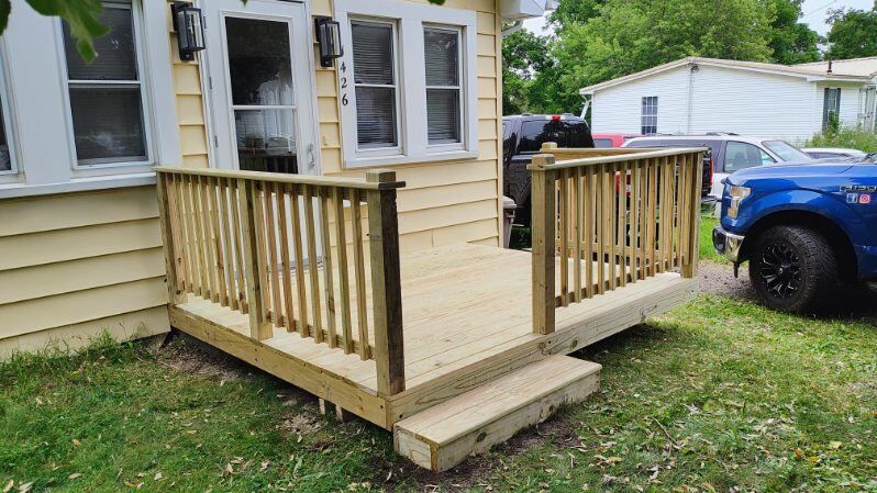 A blue truck is parked in front of a house with a wooden deck.