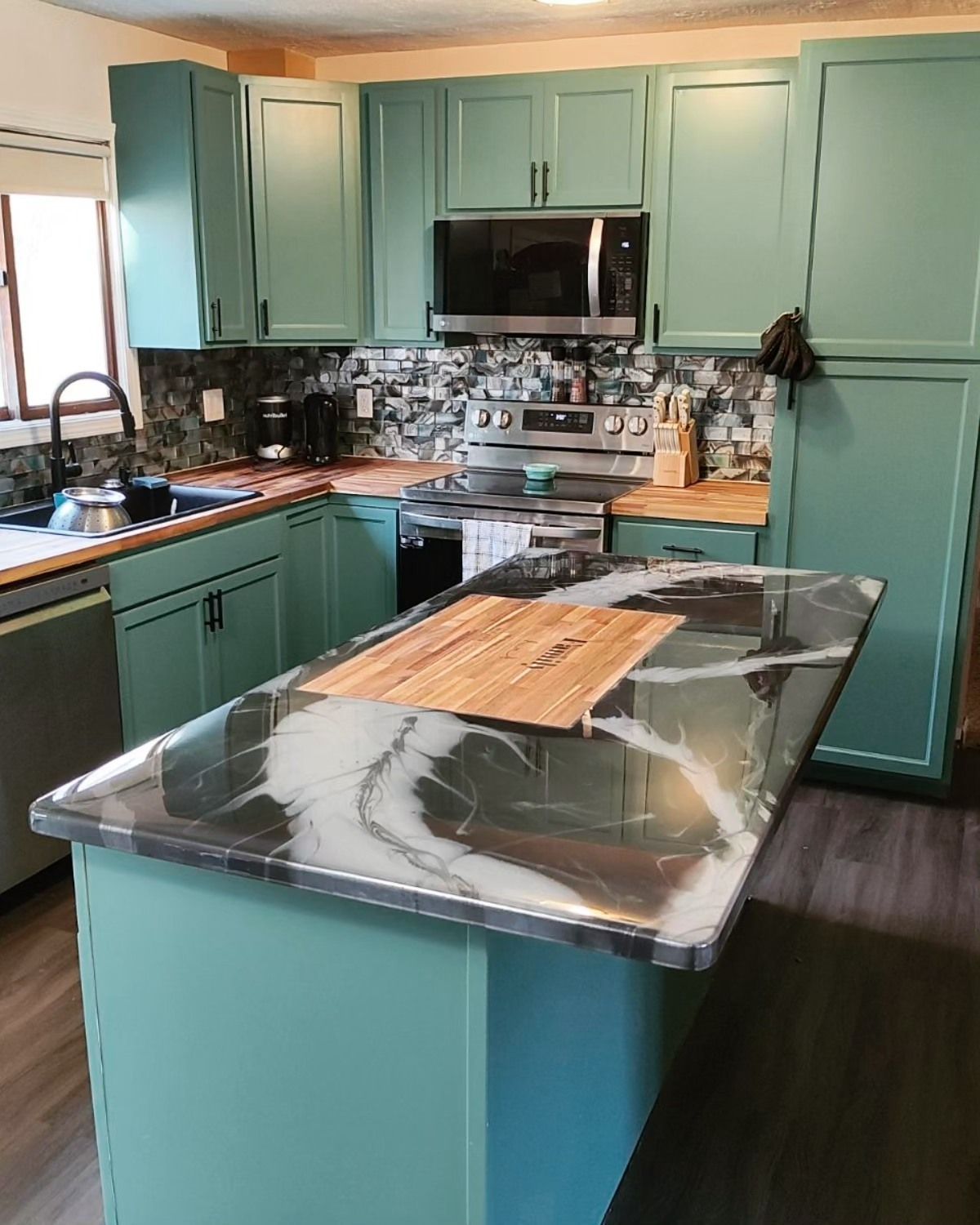A kitchen with green cabinets and a black counter top.