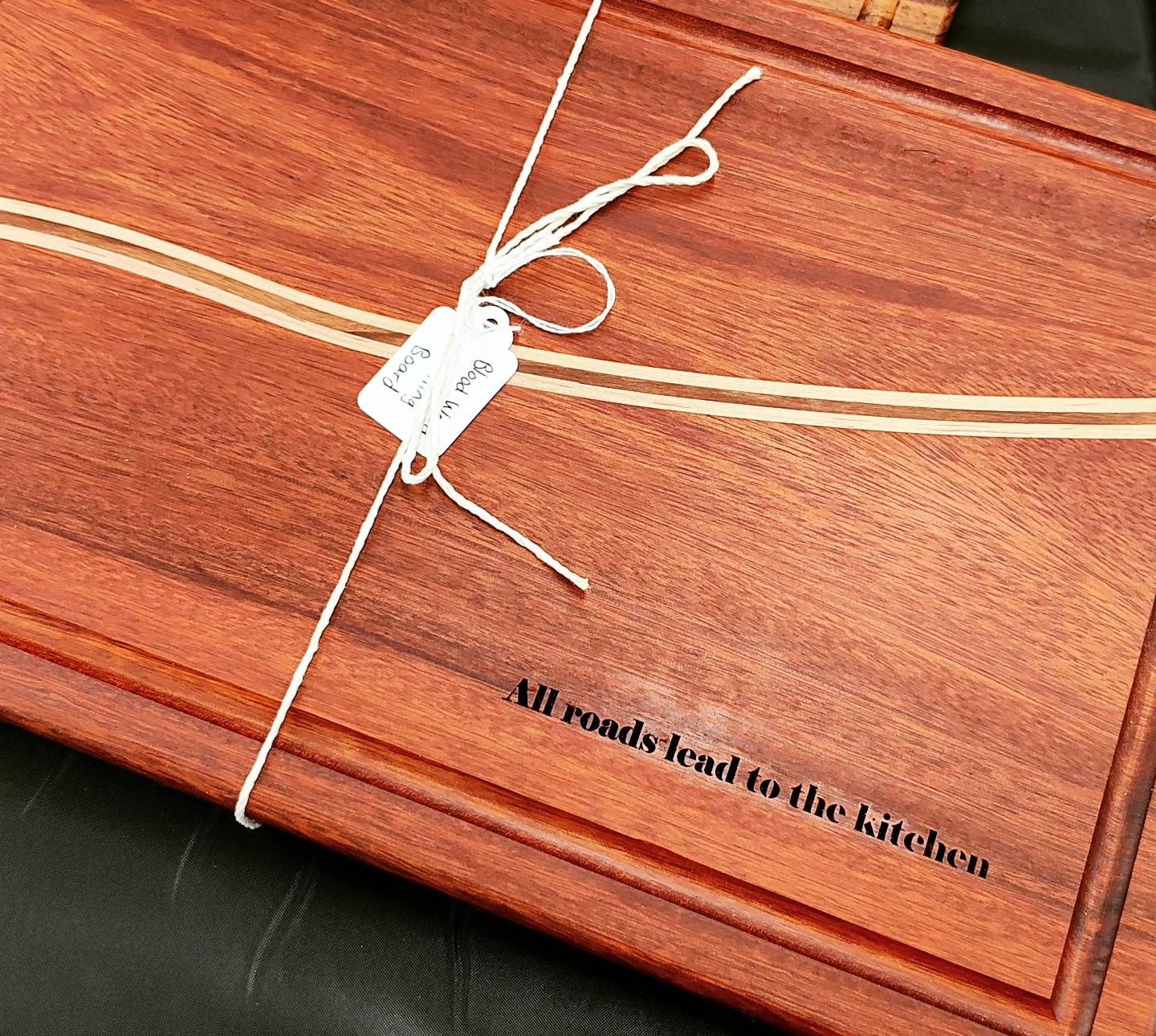 A wooden cutting board with the words all roads lead to the kitchen engraved on it