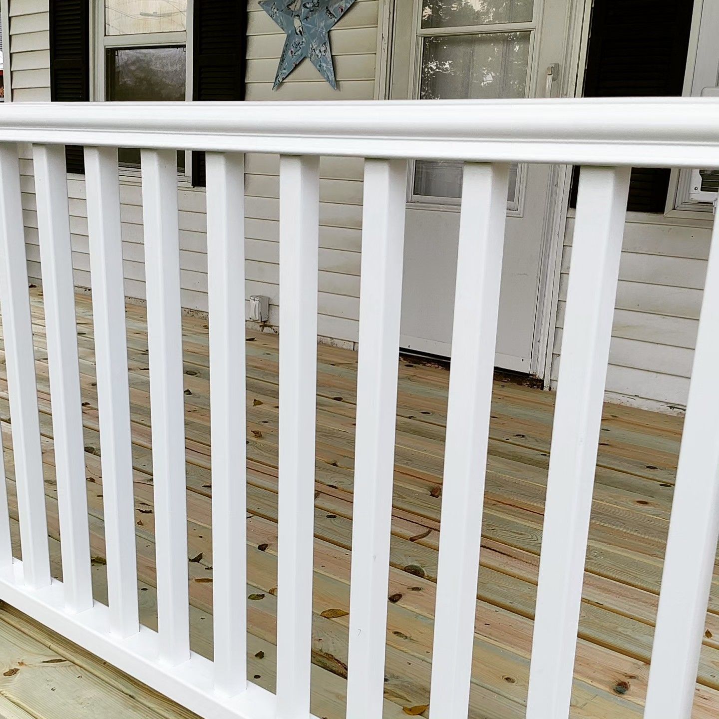 A white railing on a wooden deck in front of a house