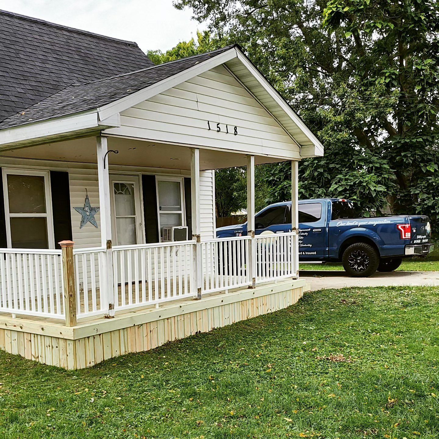 A blue truck is parked in front of a white house with a porch.
