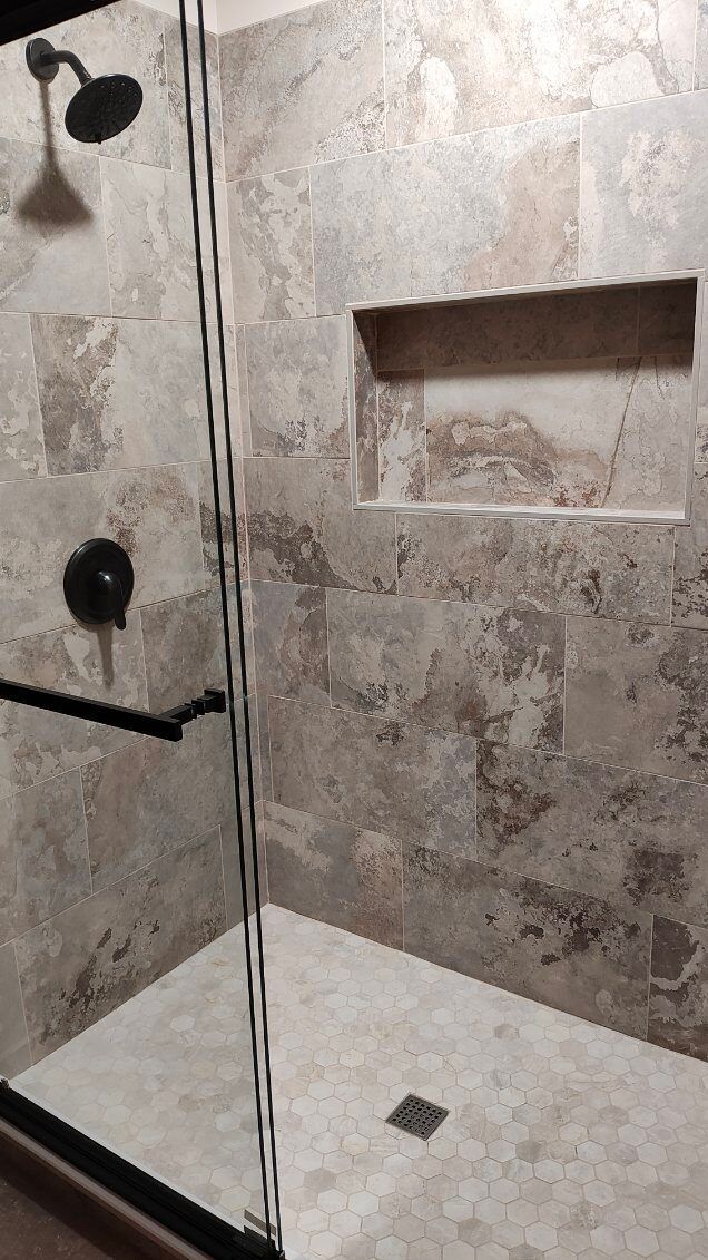 A walk in shower with a sliding glass door and a shower head.