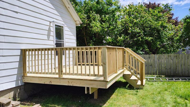 A wooden deck with stairs is in the backyard of a house.