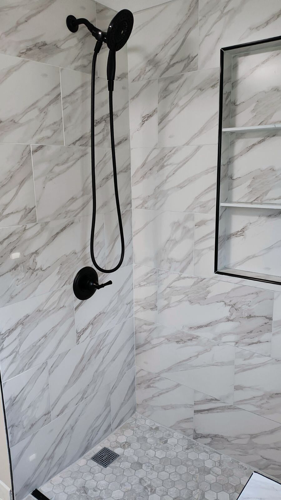A bathroom with marble walls and a walk in shower with a black shower head.