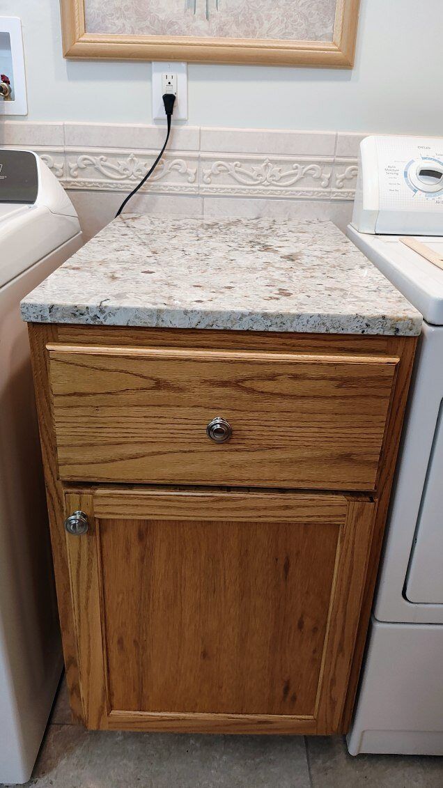 A wooden cabinet with a granite counter top in a laundry room next to a washer and dryer.