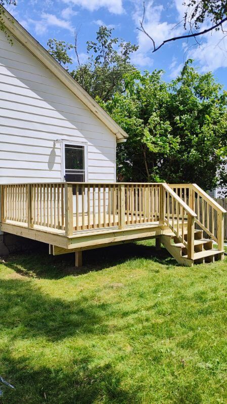 A wooden deck with stairs is in the backyard of a house.