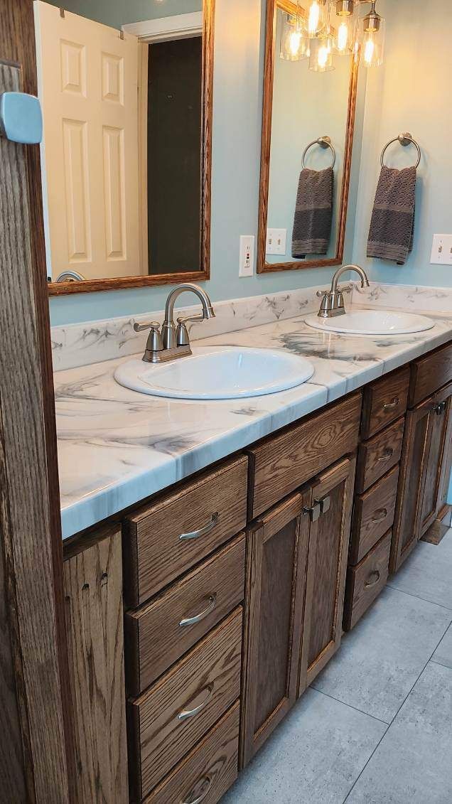 A bathroom with two sinks , two mirrors , and wooden cabinets.