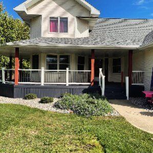 A white house with a large porch and a red jeep parked in front of it.