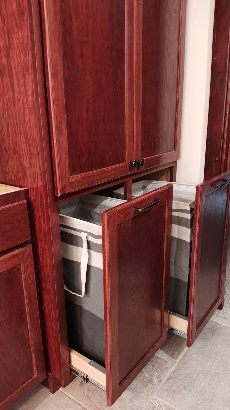 A laundry basket is pulled out of a cabinet in a kitchen.