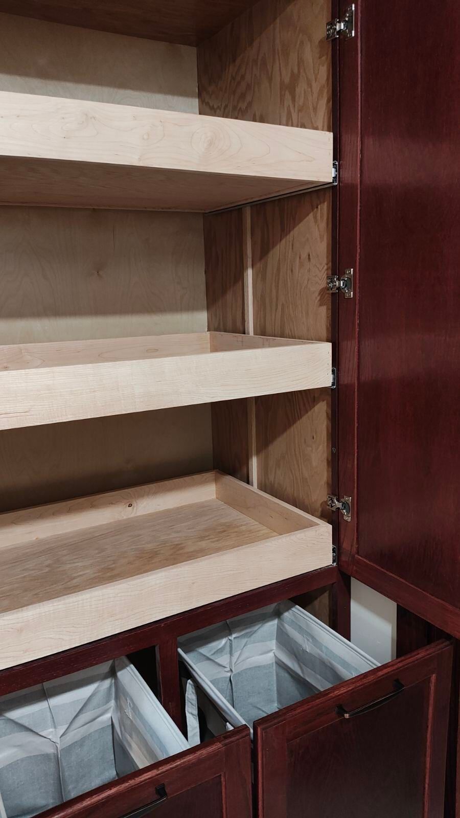 The inside of a cabinet with the door open and shelves and drawers.