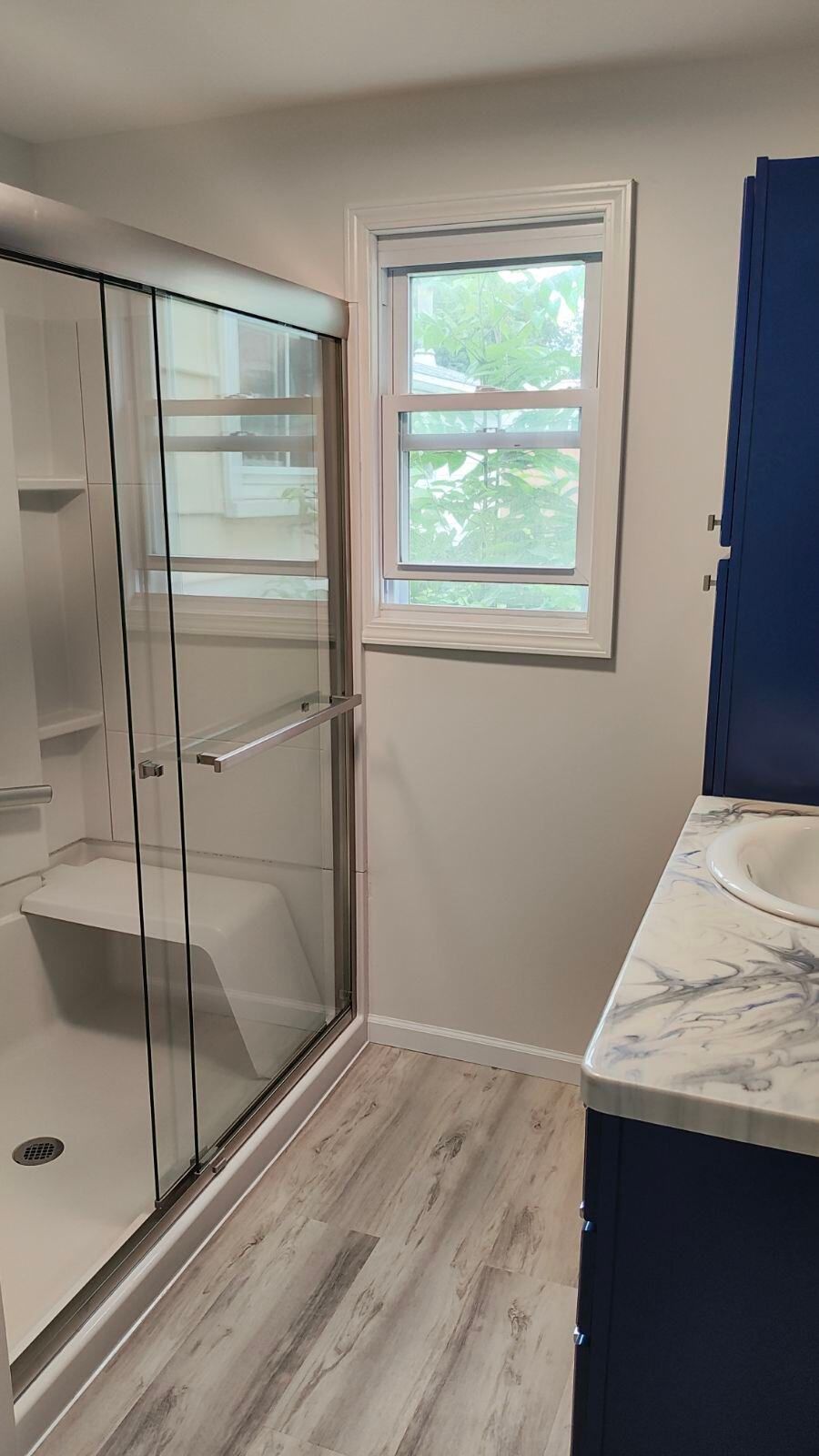A bathroom with a walk in shower , sink , and window.