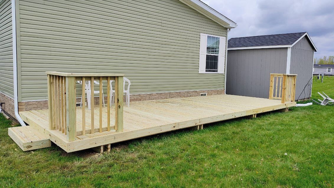 A wooden deck is sitting in the grass in front of a house.