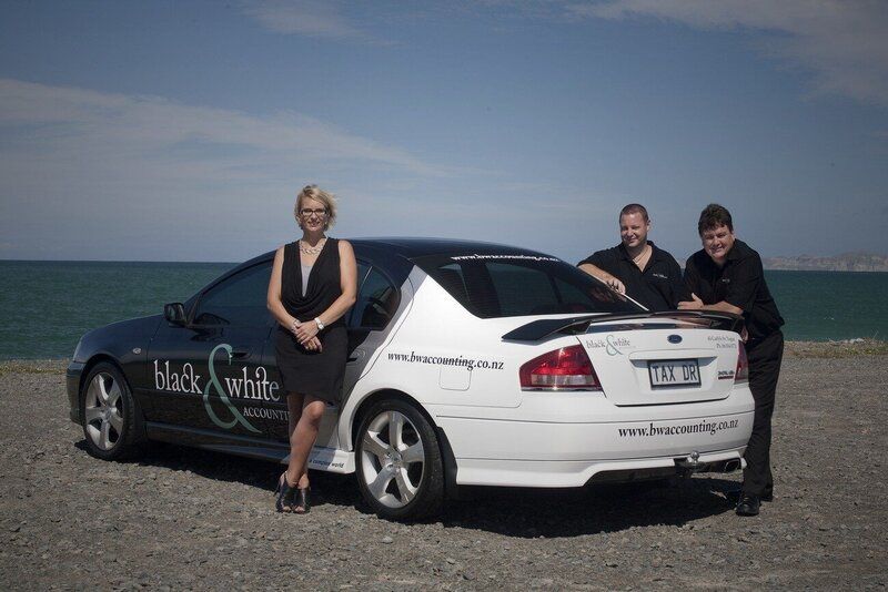 Three people standing next to a black and white car