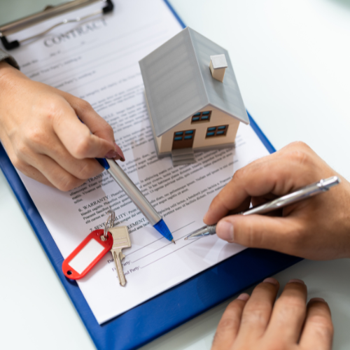 A person is signing a contract with a model house in the background