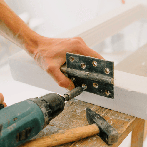 A person is using a drill to fix a door hinge.
