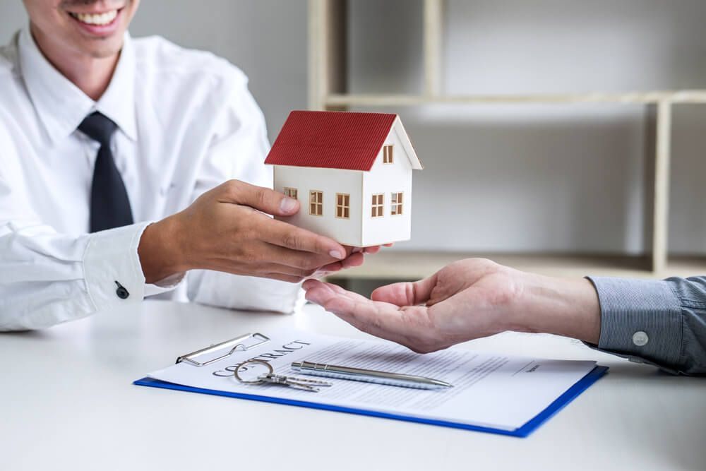 Man Hands Miniature House To Another Person; Real Estate Transaction