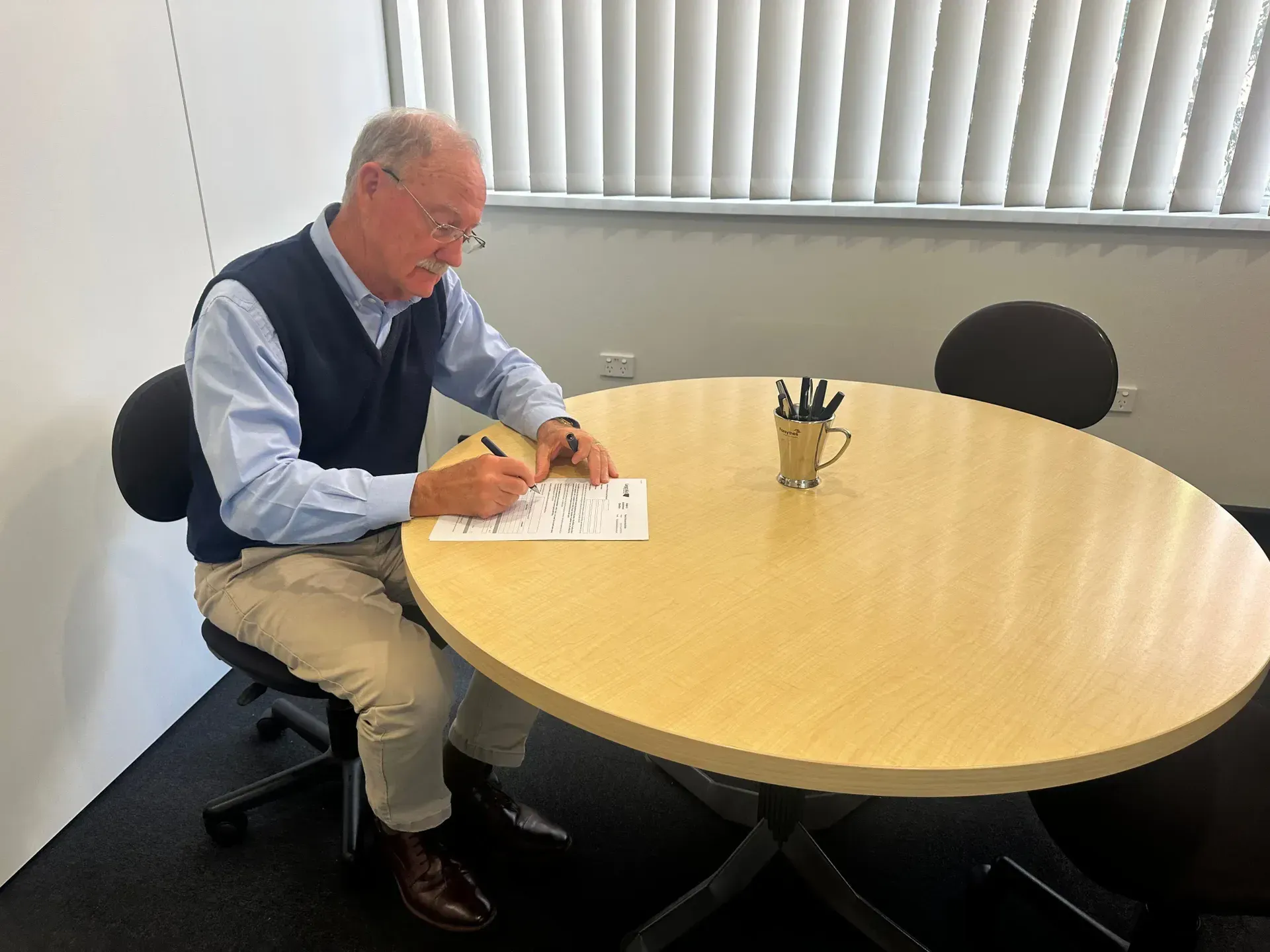 A Man is Sitting at a Round Table Writing on a Piece of Paper — Morris Legal & Conveyancing in Forster, NSW