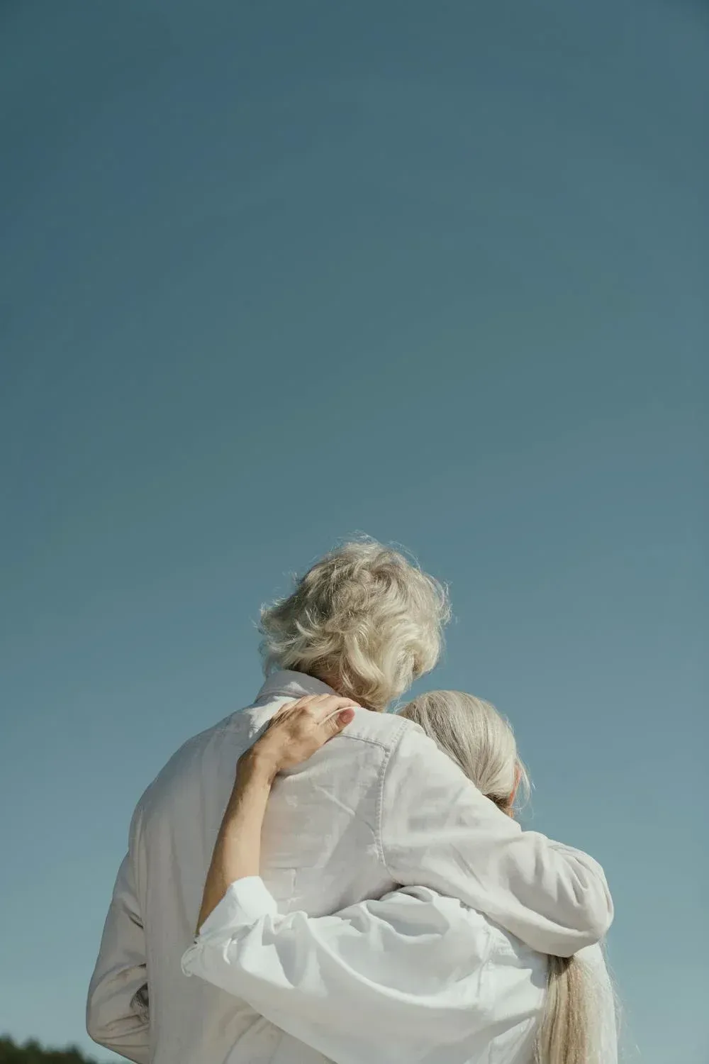 A man and a woman are hugging each other in front of a blue sky.