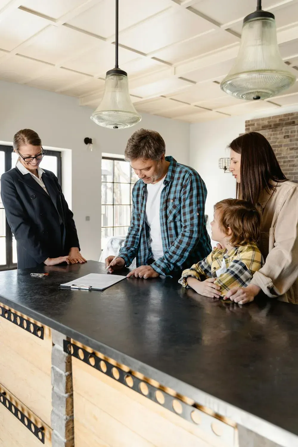 A family is signing a contract in a kitchen while a real estate agent looks on.
