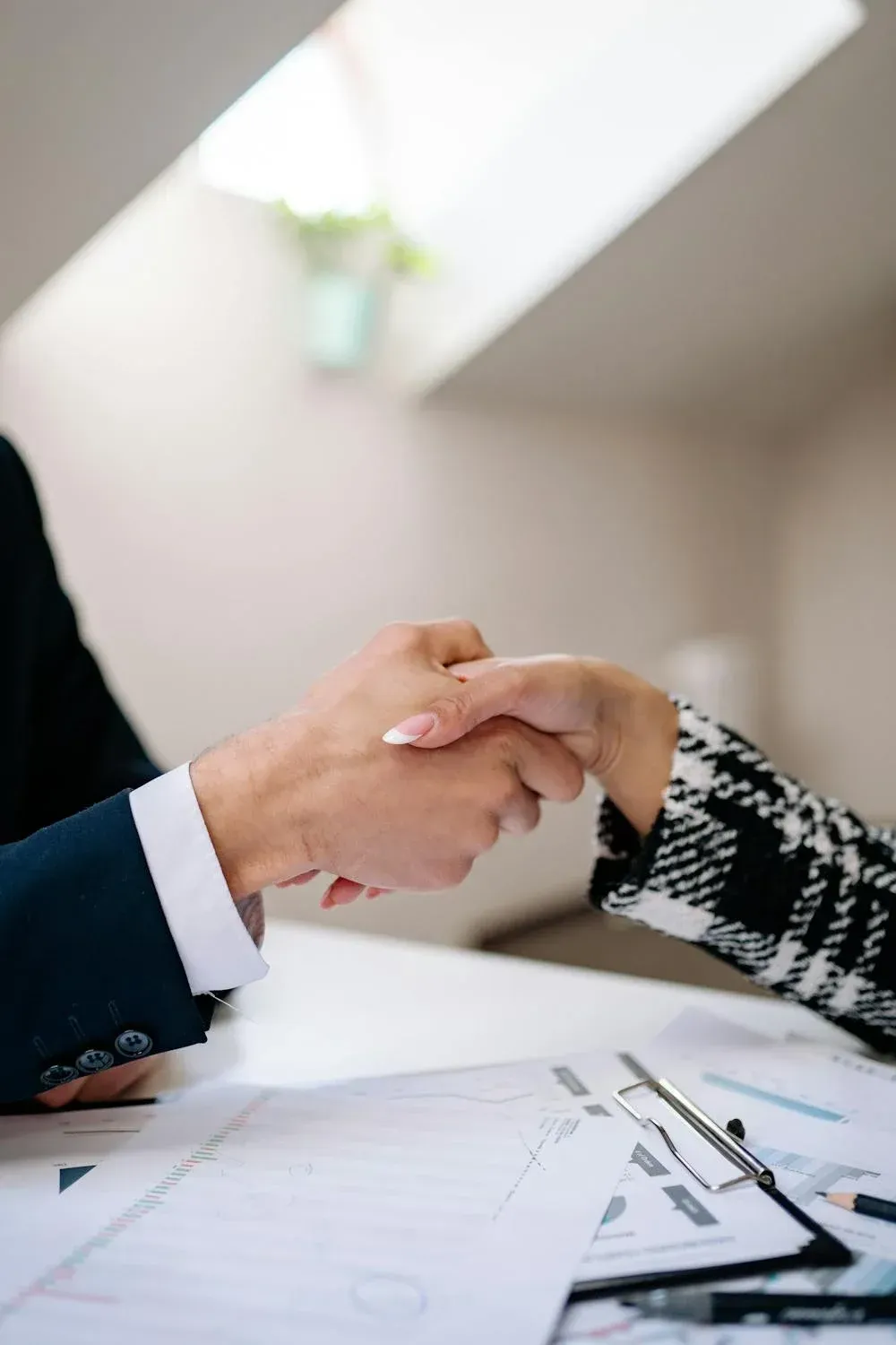 A man and a woman are shaking hands over a table.