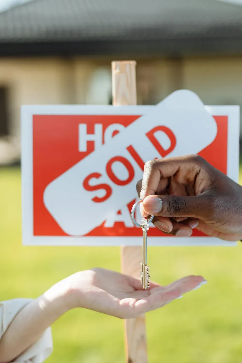 A person is holding a key in front of a sold sign.
