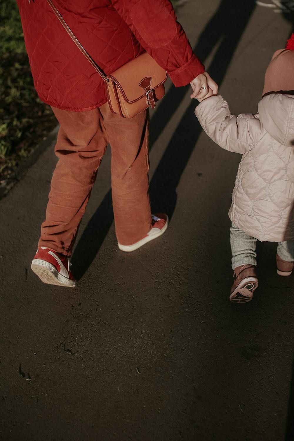 A woman is holding a child 's hand while walking down the street.