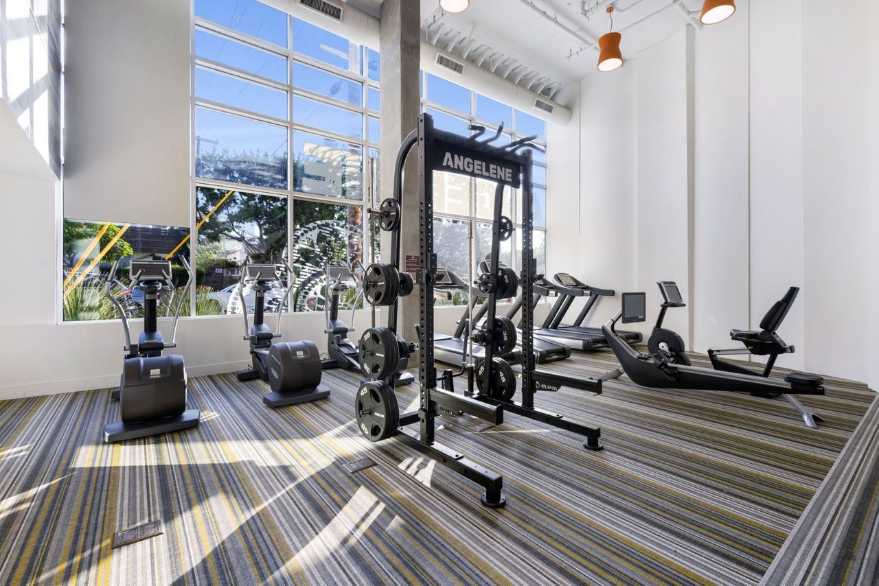 Angelene Apartments Fitness center with weight rack, cardio machines, and large windows.