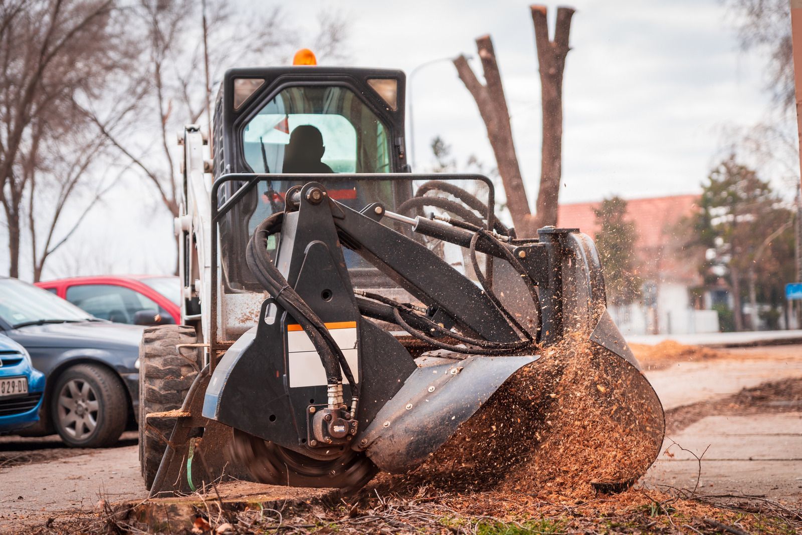 A tractor is stump grinding a tree in a parking lot.