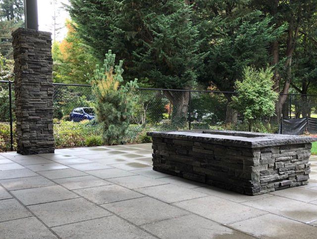 A fire pit is sitting on a patio next to a stone wall.