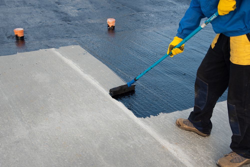 A man is painting a concrete surface with a broom.