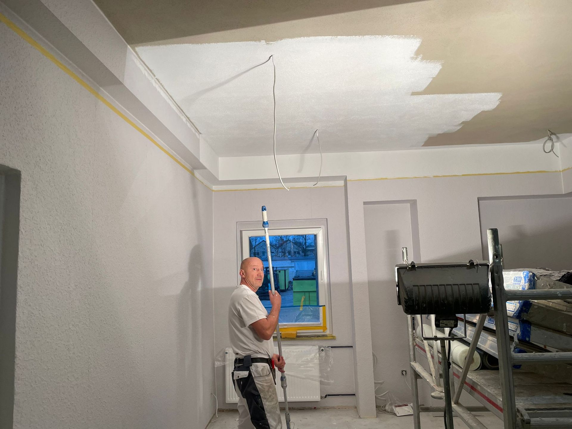 Ein Mann streicht die Decke eines Zimmers.