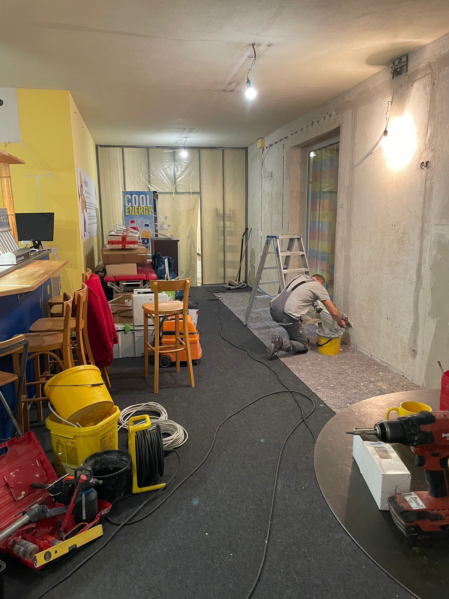 Ein Mann arbeitet mit vielen Werkzeugen in einem Raum an einer Wand.