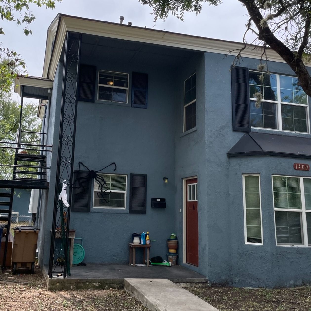Two-story blue stucco building with black shutters and a red door. Exterior metal staircase on the left.