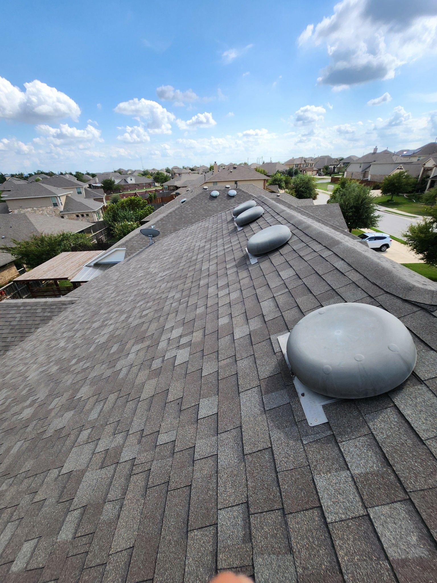 Gray shingled roof with multiple round vents, blue sky background, residential setting.