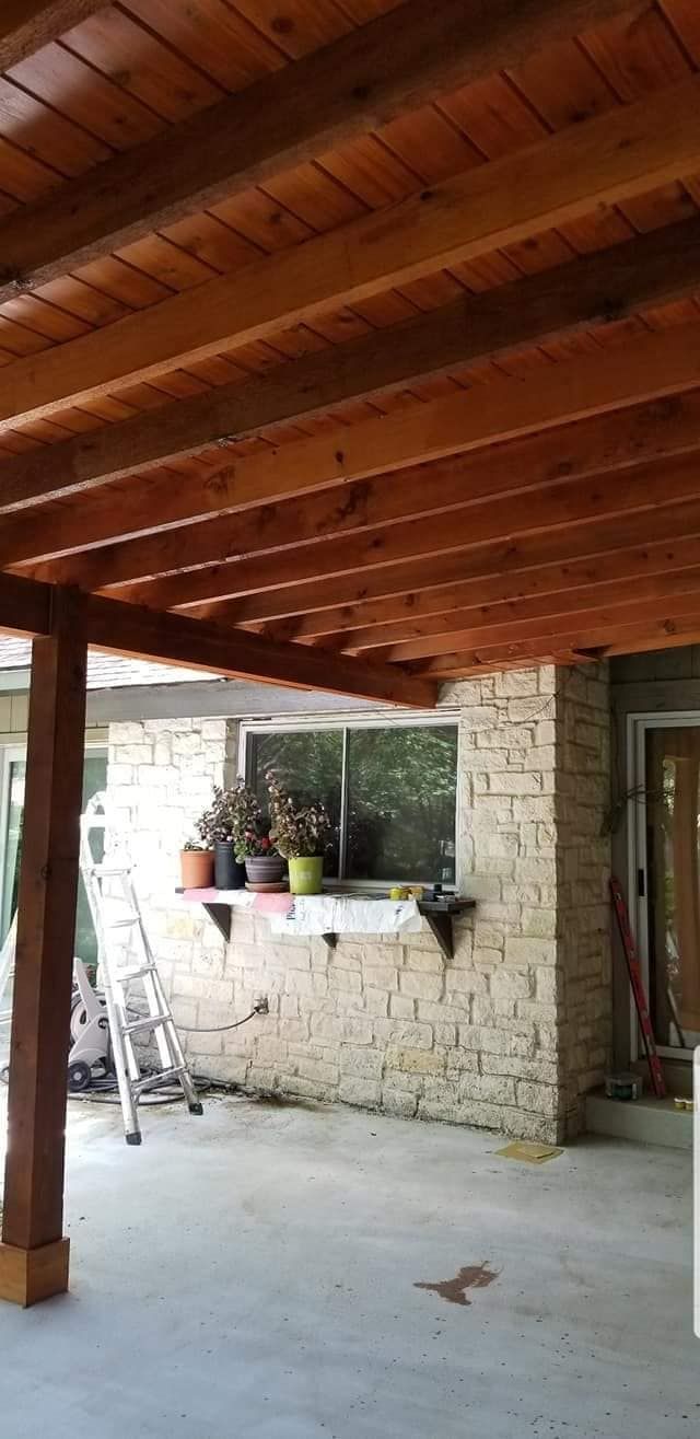 View from a patio with wood plank ceiling, brick wall, window, plants, and a ladder.