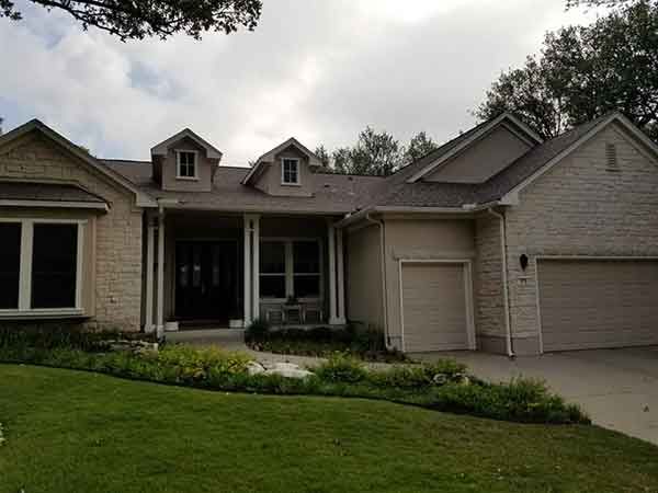 Beige brick house with garage and front porch, set on a green lawn under a cloudy sky.