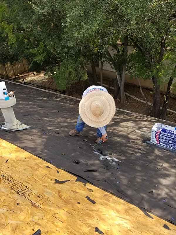 Person with straw hat working on a rooftop, near trees.