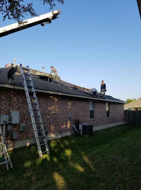 Roofers working on a brick house roof with a ladder and lift on a sunny day.