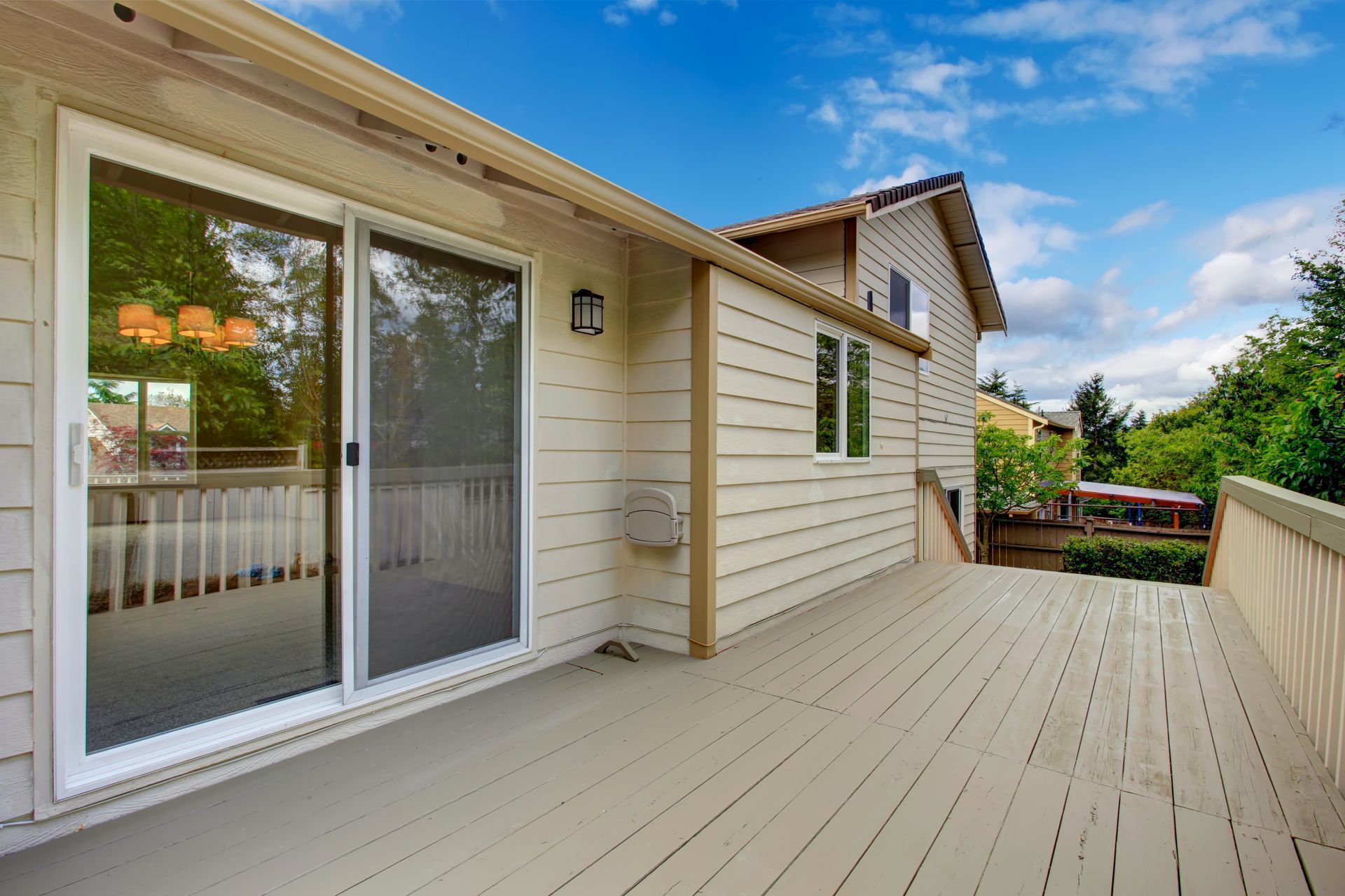 Beige house with sliding glass door onto a wooden deck, blue sky above.